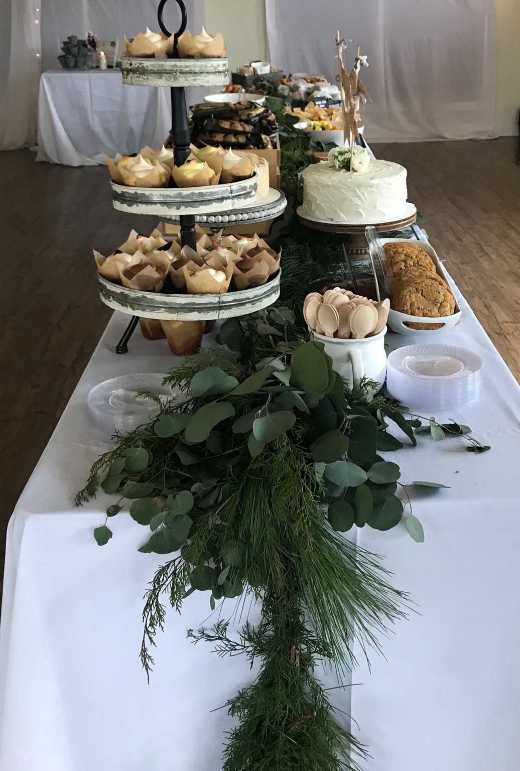 Baby shower dessert table with white cake, cupcakes and fresh eucalyptus garland