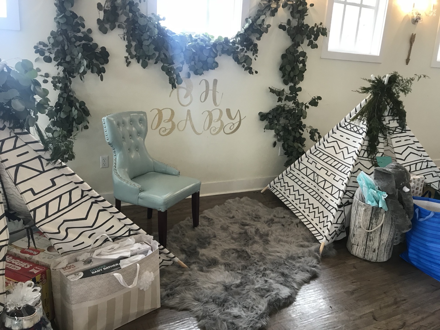 Oh Baby lounge with two patterned teepees, eucalyptus greenery and a soft gray rug