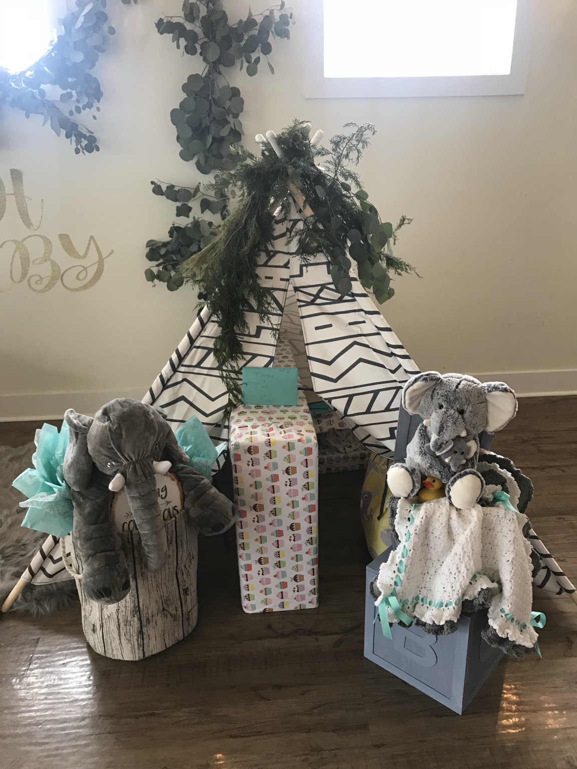 Baby shower teepee gift display with elephant toys and eucalyptus greenery